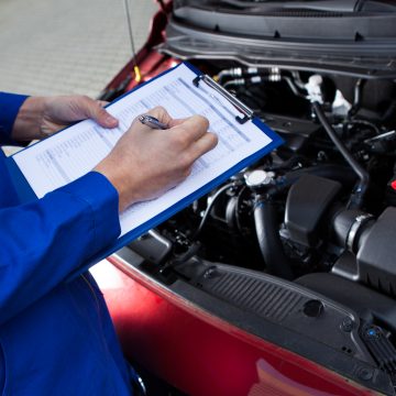 Midsection of mechanic holding clipboard in front of open car engine at street